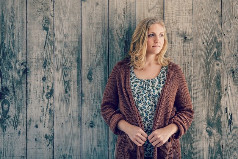 blonde woman standing near wooden wall