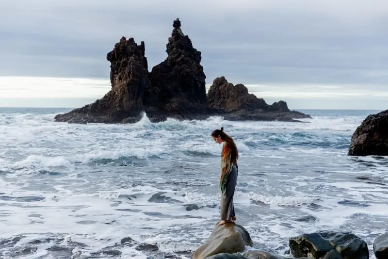 woman in dress standing on rock near sea