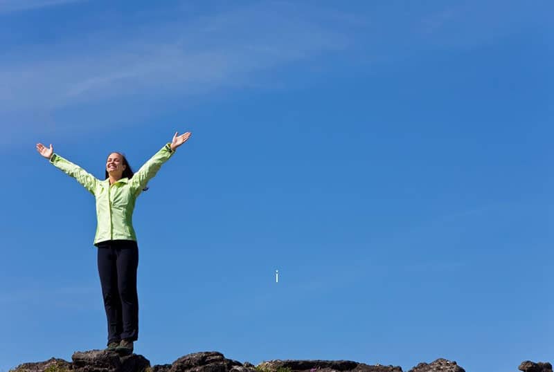 woman stands on the horizon arms raised celebrating for reaching the top of the mountain