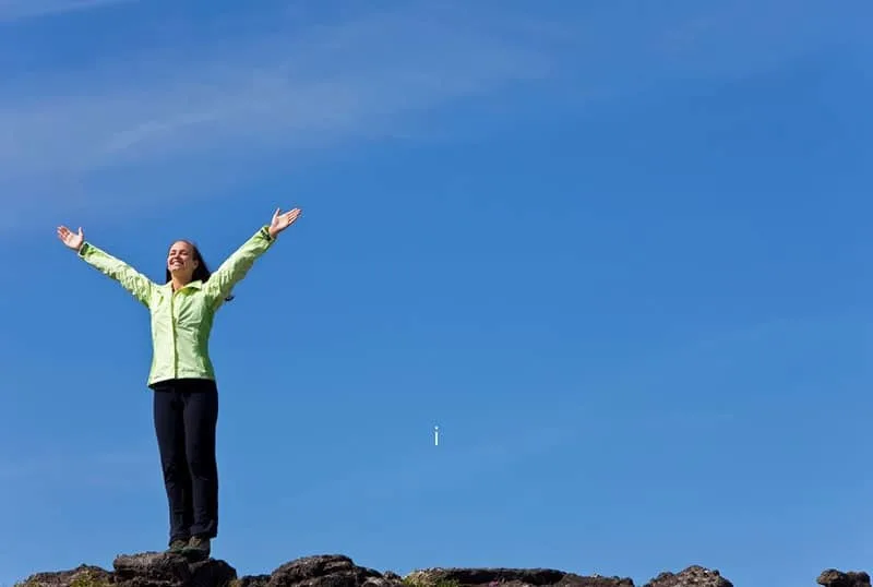 woman stands on the horizon arms raised celebrating for reaching the top of the mountain