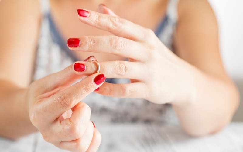 Hands of woman with red nail polish taking wedding ring off