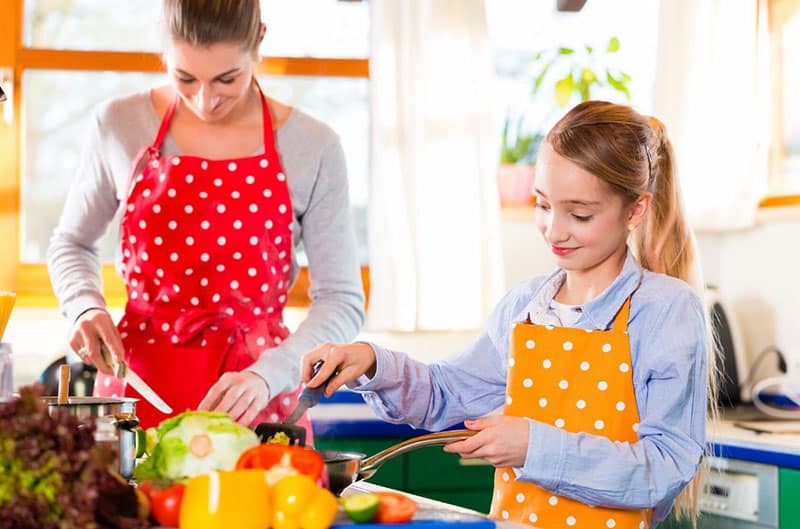 mulher a ensinar um miúdo a cozinhar na cozinha com aventais