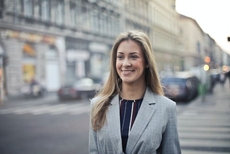 mujer sonriente con abrigo gris caminando por la calle