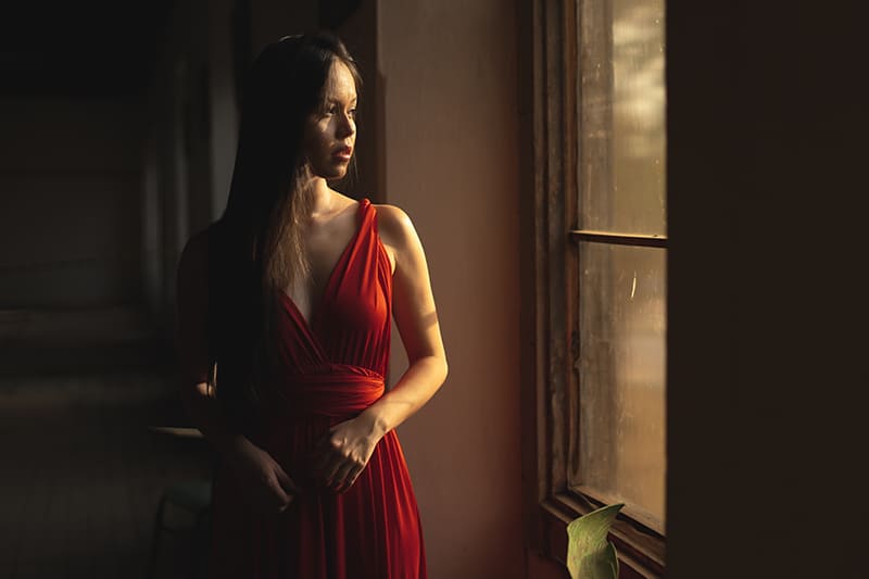 mujer con vestido rojo cerca de una ventana