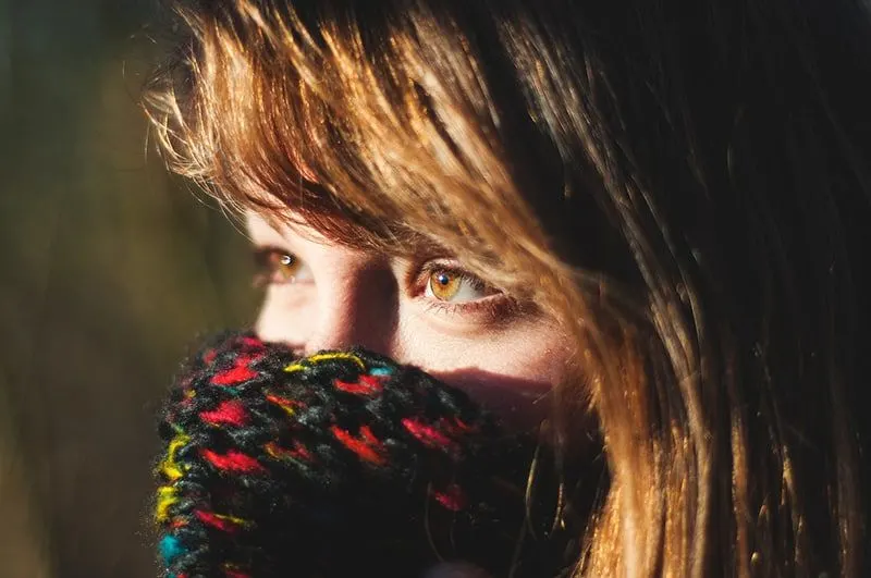 woman with brown eyes covering her mouth with knit scarf
