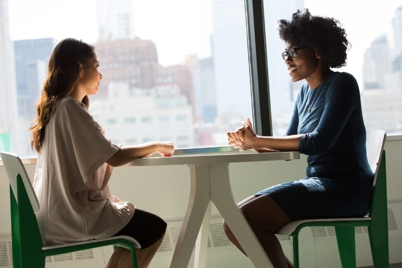 duas mulheres sentadas em cadeiras ao lado da janela