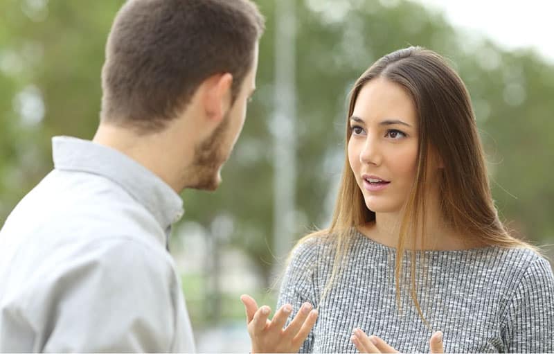 joven pareja discutiendo al aire libre con árboles verdes en desenfoque