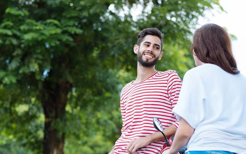 joven pareja coqueteando al aire libre cerca de un árbol