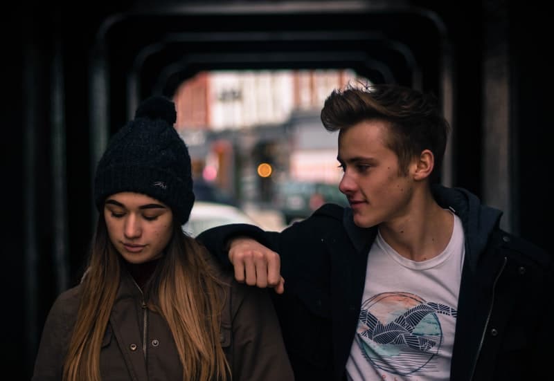 young couple in city at night with man's arms of woman's shoulder