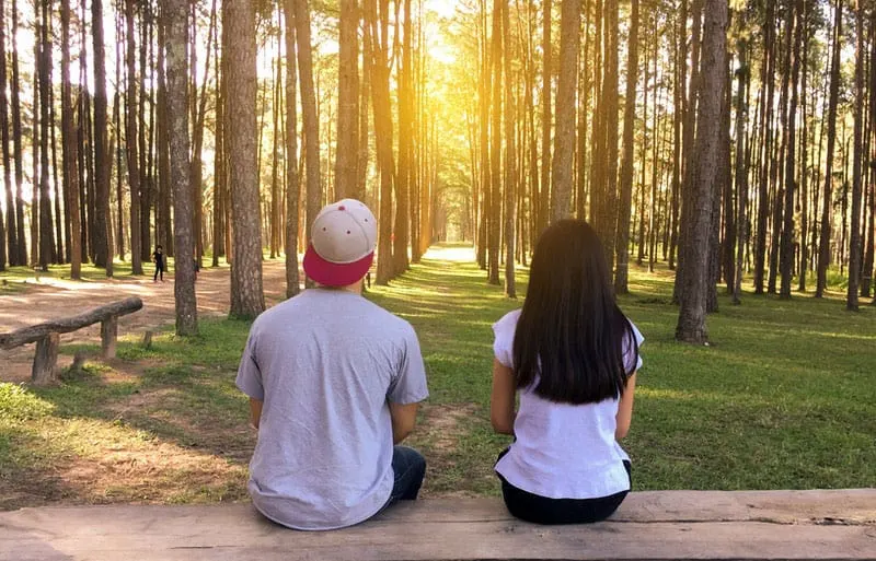 young couple sitting in the wooden bench in the middle of the countryside forest