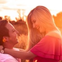 homem sorridente ao colo de uma mulher com um top cor-de-rosa