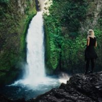 blonde woman standing in front of waterfall