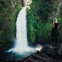 mujer rubia de pie frente a una cascada