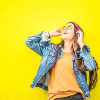 smiling woman in denim jacket standing near yellow wall