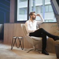 pensive man sitting near the windows alone with one leg placed over the other