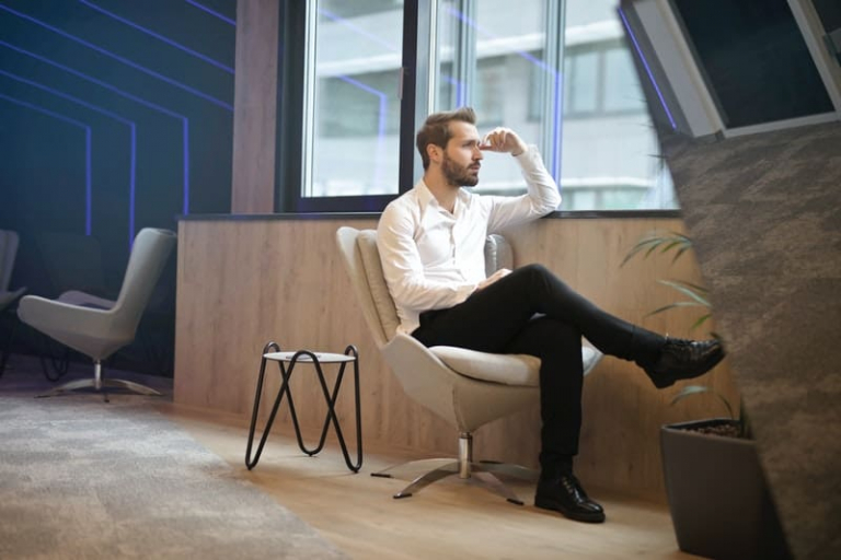 pensive man sitting near the windows alone with one leg placed over the other