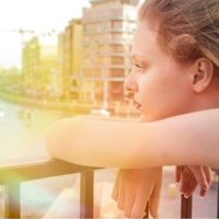 pensive woman leaning on the railings facing a body of water with rainbow colors scheme of lights from camera