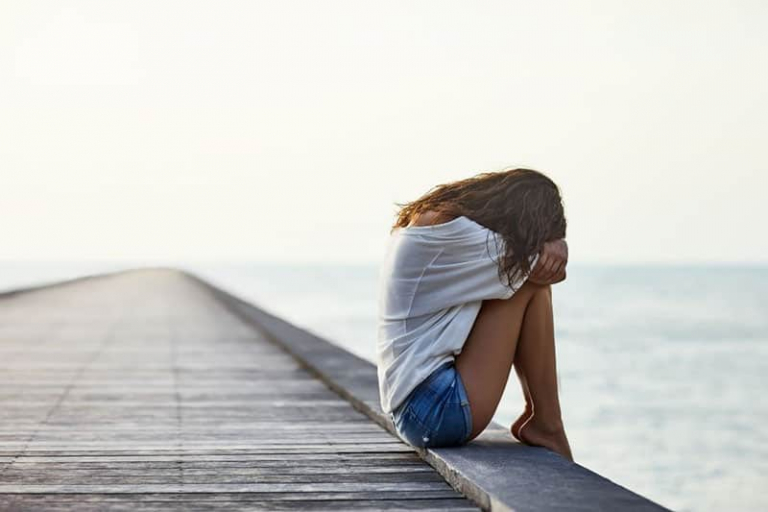 woman crying sitting in the edge of a wooden walkway near a body of water