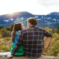 man and woman sitting on rock facing mountain