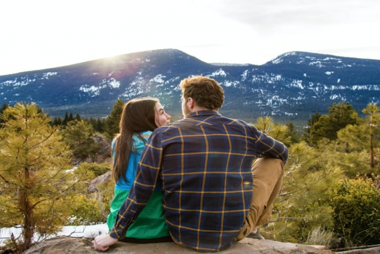 man and woman sitting on rock facing mountain