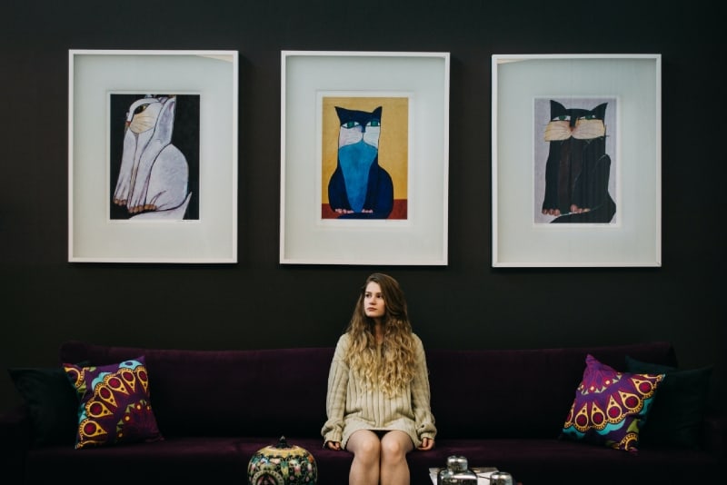 woman sitting on brown sofa above three cat paintings