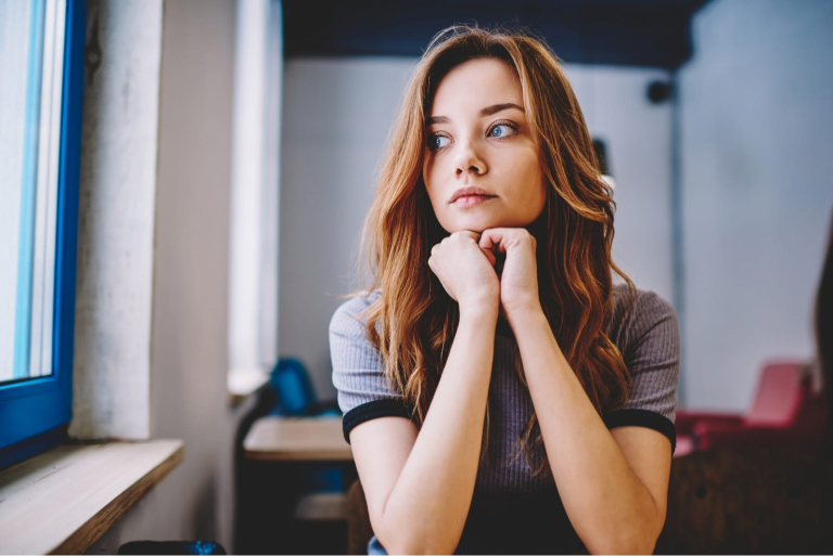 beautiful young woman sitting by the table looking out of window
