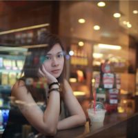 a sad Asian woman is sitting in a cafe behind the bar by the window