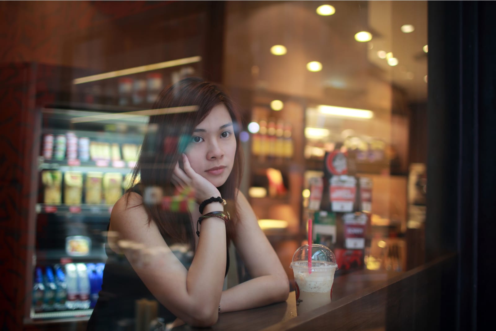 a sad Asian woman is sitting in a cafe behind the bar by the window