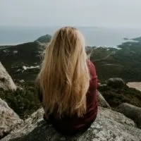 blonde woman sitting on rock looking at sea