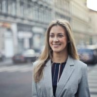 mujer rubia sonriente con abrigo cruzando la calle