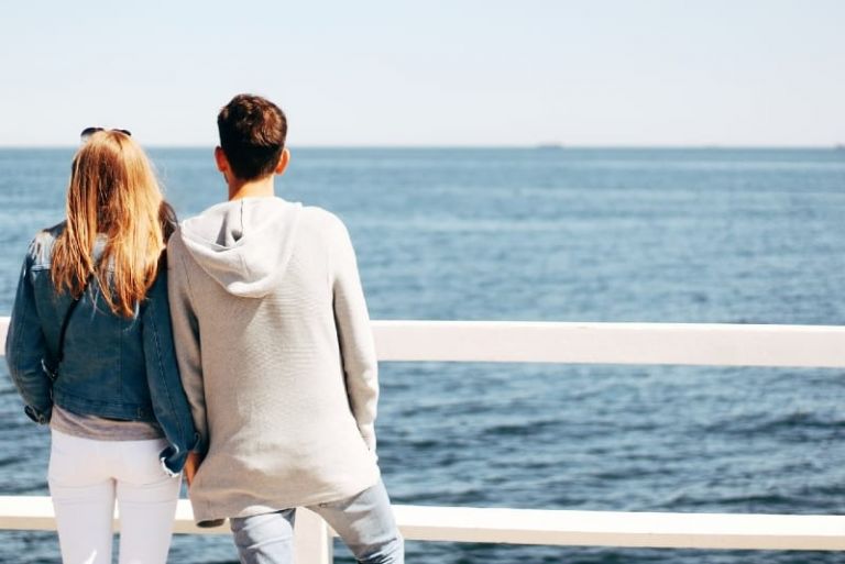 man and woman holding hands looking at sea