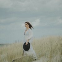 woman in white shirt holding hat while standing in field