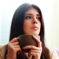 pensive woman sitting while holding a coffee cup