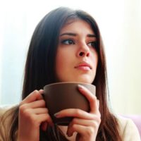 mujer pensativa sentada con una taza de café en la mano