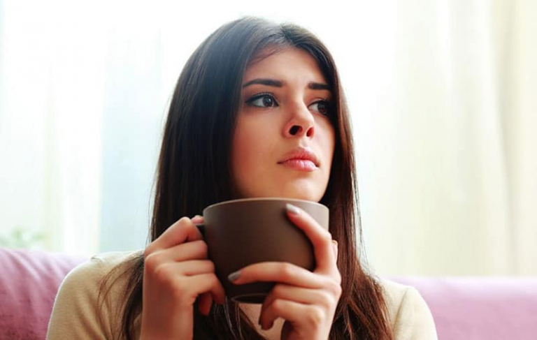 pensive woman sitting while holding a coffee cup