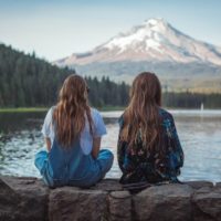 two women sitting on rock looking at water