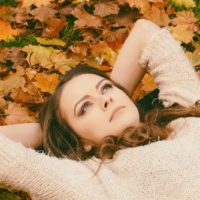 pensive young woman lying in the dried leaves during autumn season