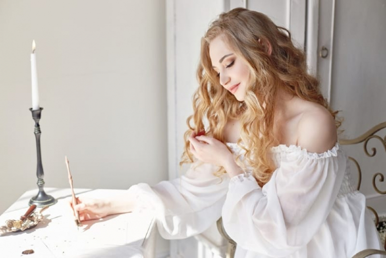 woman in white off-shoulder top writing letter at table