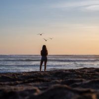 mulher de pé na praia a olhar para o mar