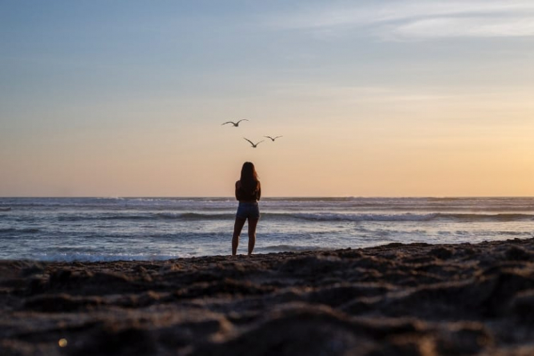 woman standing on shore looking at sea