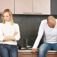 pareja preocupada no hablar el uno al otro dentro de la cocina con el hombre sentado en el fregadero cerca de la mujer