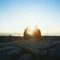 homem e mulher sentados numa rocha durante o nascer do sol