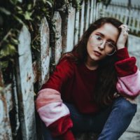 woman with eyeglasses sitting near wooden fence