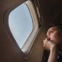 mulher sentada perto da janela de um avião a olhar para o exterior