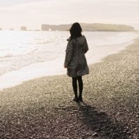 donna in piedi sulla spiaggia che guarda il mare
