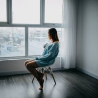 mujer con jersey azul sentada en una silla cerca de una ventana