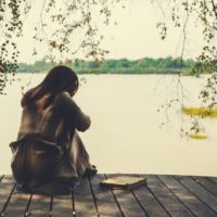 donna sola e triste seduta in riva al lago