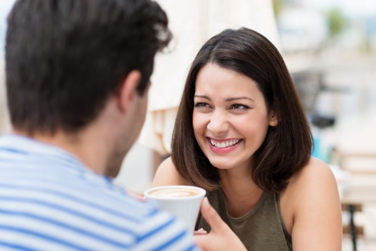 smiling woman holding cup of coffee looking at man