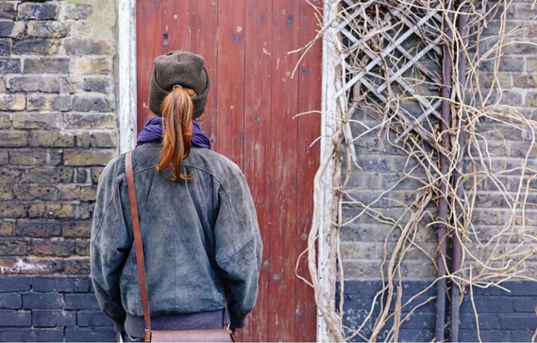 woman standing before the closed door wearing cap and denim jacket with a bag