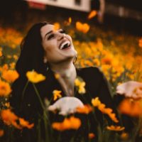 woman laughing while sitting on yellow flower field